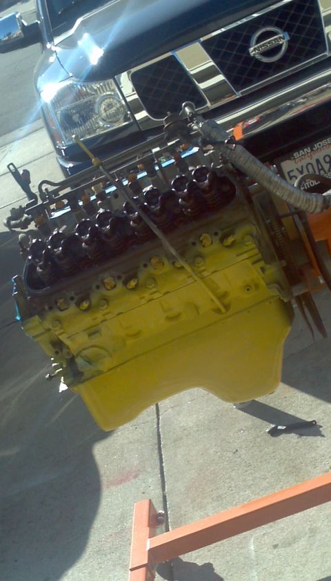 1987 Ford Bronco - Engine on stand in front of a Nissan Titan truck. The engine is painted yellow.