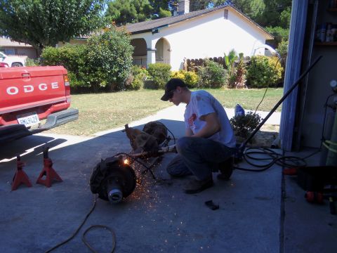 1968 Ford Bronco - A person works on a vehicle differential with sparks flying, while a red Dodge pickup truck is parked nearby.