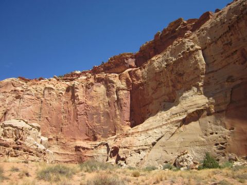 1991 Ford LTD Crown Victoria - Vast sandstone cliffs dominate the landscape under a bright blue sky, with sparse desert plants dotting the sandy ground.