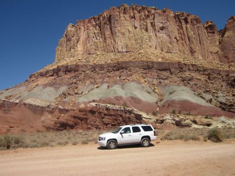 1991 Ford LTD Crown Victoria - White SUV parked near a massive, colorful rock formation under a clear blue sky.