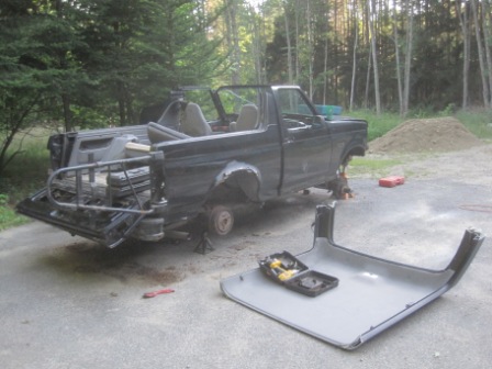 1993 Ford Bronco - A disassembled Ford Bronco sits outside, with its roof panel removed and placed on the ground.