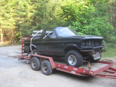 1993 Ford Bronco - A black Ford Bronco is being transported on a trailer, missing its front grille and bumper.