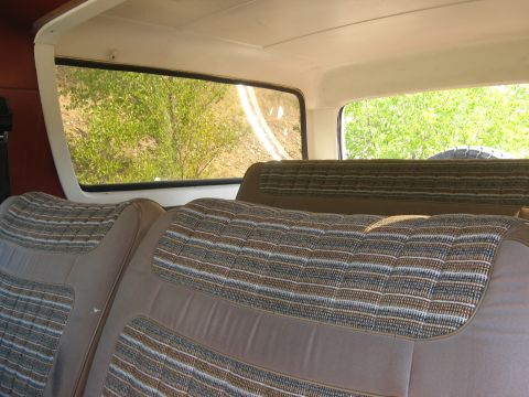 1981 Ford Bronco - The interior of a vehicle shows patterned seats and a view of a dirt road through the rear window.