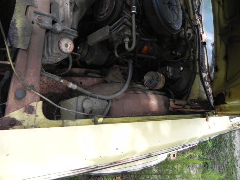 1974 Ford Ranchero - The engine bay of a yellow vehicle shows signs of rust and wear, with various hoses and components visible.