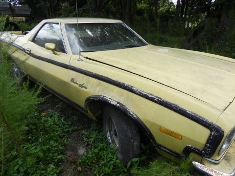 1974 Ford Ranchero - A yellow 1974 Ford Ranchero sits in overgrown grass, showing its distinctive side profile and fender badging.