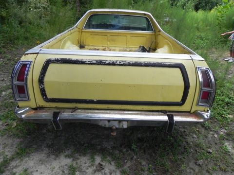1974 Ford Ranchero - The rear of a yellow pickup truck with a chrome bumper and a tow hitch is shown in an outdoor setting.