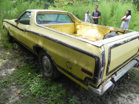 1974 Ford Ranchero - A yellow 1974 Ford Ranchero sits in overgrown grass, viewed from the rear three-quarter perspective.