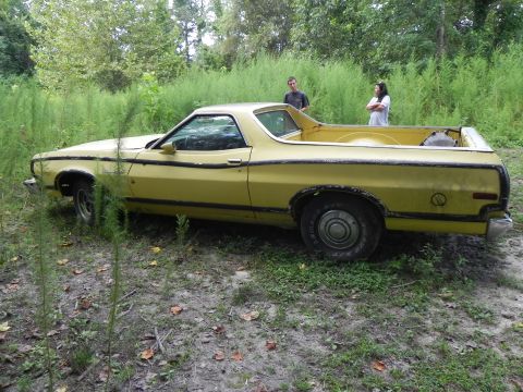 1974 Ford Ranchero - A yellow 1974 Ford Ranchero sits in an overgrown field with two people standing in the background.