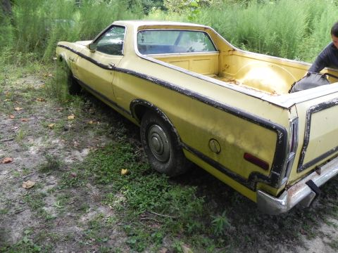 1974 Ford Ranchero - A yellow 1974 Ford Ranchero pickup truck sits in overgrown grass, showing its rear passenger side.