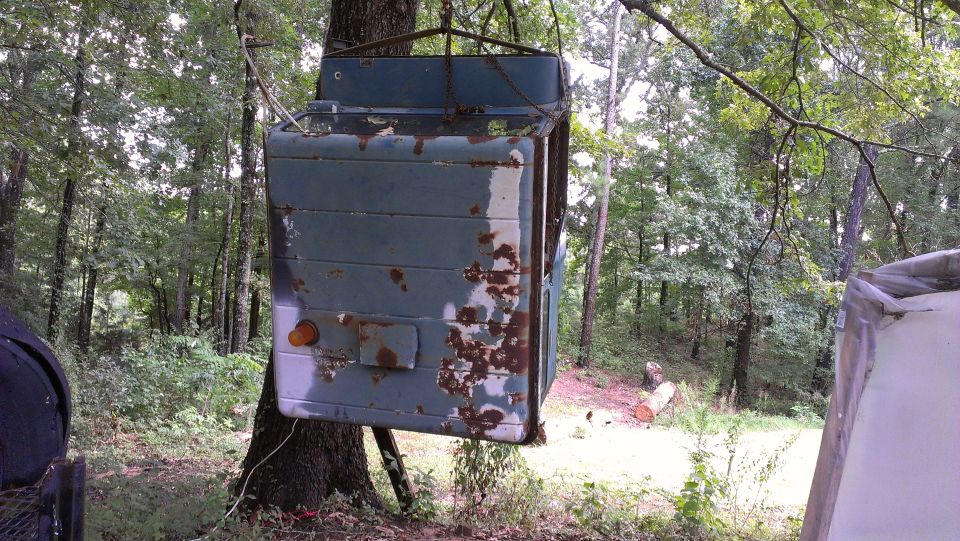Rusted blue truck cab hanging from a tree in a wooded area