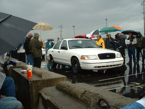1999 Ford Crown Victoria - A white 1999 Ford Crown Victoria is shown from the front during an outdoor auction on a rainy day.