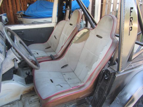 1987 Suzuki Samurai - The interior of a vehicle features worn bucket seats, a roll cage, and a steering wheel, with visible text on a panel.