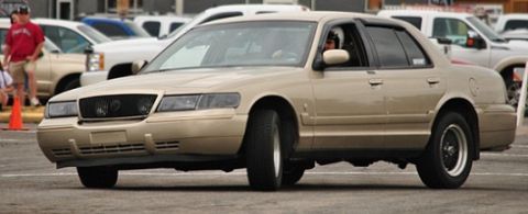 2000 Mercury Grand Marquis - A tan 2000 Mercury Grand Marquis sedan is captured in motion, with its driver visible behind the wheel.