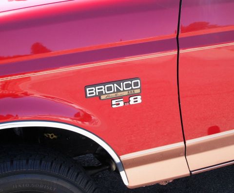 1994 Ford Bronco - Close-up of a red Ford Bronco's front fender showing the "BRONCO 5.8" badge with an "Eddie Bauer" script and tan tri-stripe insert, above t…
