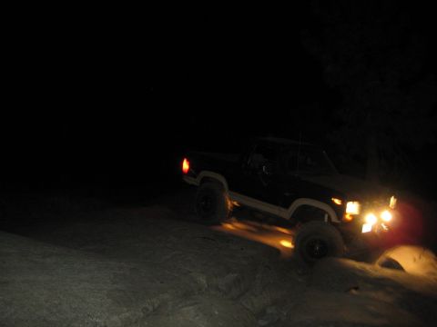 1986 Ford Bronco - A truck navigates a rocky terrain in the dark, illuminated by its headlights.