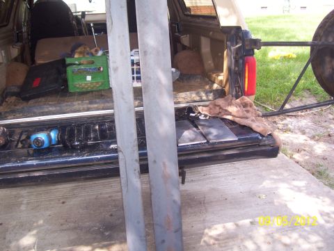 1990 Ford Bronco - Pickup truck tailgate loaded with tools and metal parts, with a spare tire mounted outside.