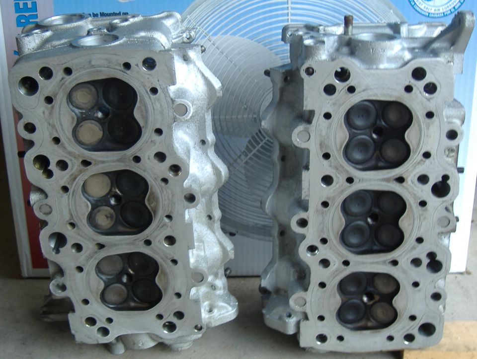 Two aluminum engine cylinder heads with valves visible, one on the left and one on the right