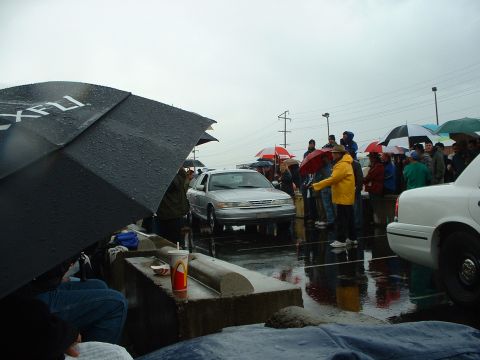1999 Ford Crown Victoria - A silver sedan is viewed from the front at an outdoor event with many people holding umbrellas.