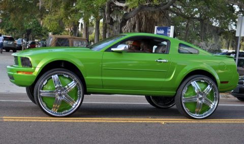 2007 Ford Mustang - A lime green Ford Mustang with custom large chrome wheels is driven on a street.
