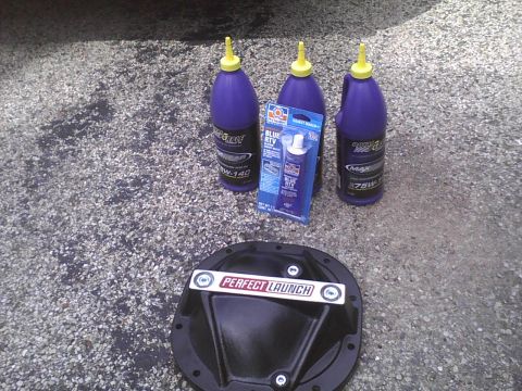 2003 Ford Crown Victoria - Automotive parts including a differential cover, gear oil, and sealant are laid out on a gravel surface.