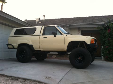 1985 Toyota Pickup/SR5 - This modified pickup truck features oversized tires and a camper shell, parked in front of a residential garage.
