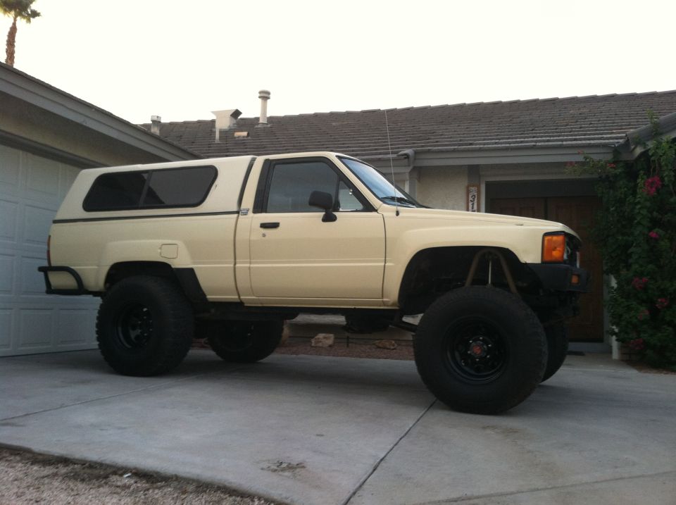 Lifted beige pickup truck with a white camper shell, parked in a driveway