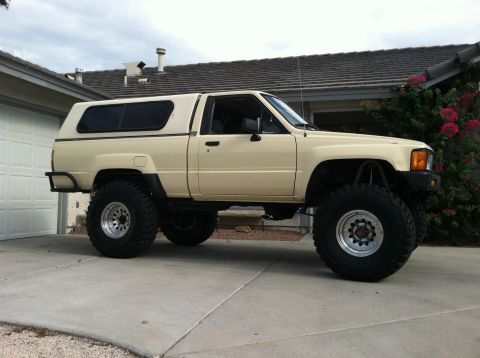 1985 Toyota Pickup/SR5 - This lifted Toyota pickup truck, likely a 1984 model, is equipped with a camper shell and oversized tires.