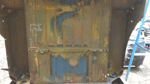 1978 Ford Bronco - The heavily rusted undercarriage of a vehicle shows chalk markings for measurements, with a large tire visible in the background.