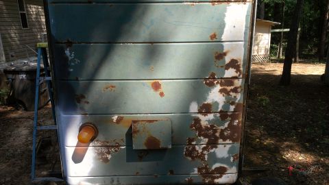 1978 Ford Bronco - The weathered side of a trailer shows extensive rust and peeling paint, with an orange marker light visible.
