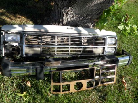 1994 Jeep Cherokee - Front end parts for a 1994 Jeep Cherokee, including the grille, headlights, and chrome bumper, laid out on grass.