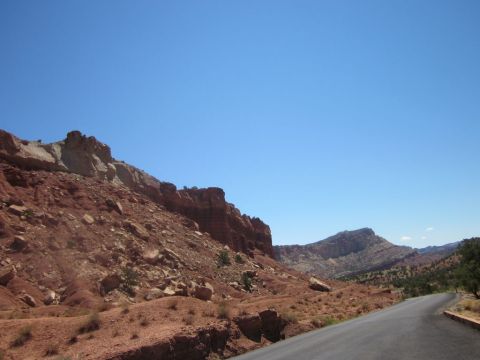 1991 Ford LTD Crown Victoria - A road winds through a desert canyon with red rock cliffs and sparse vegetation under a bright blue sky.