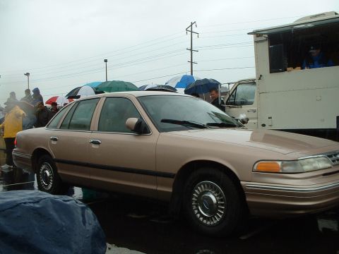 1999 Ford Crown Victoria - Tan Ford Crown Victoria sedan seen in the rain with people holding umbrellas.