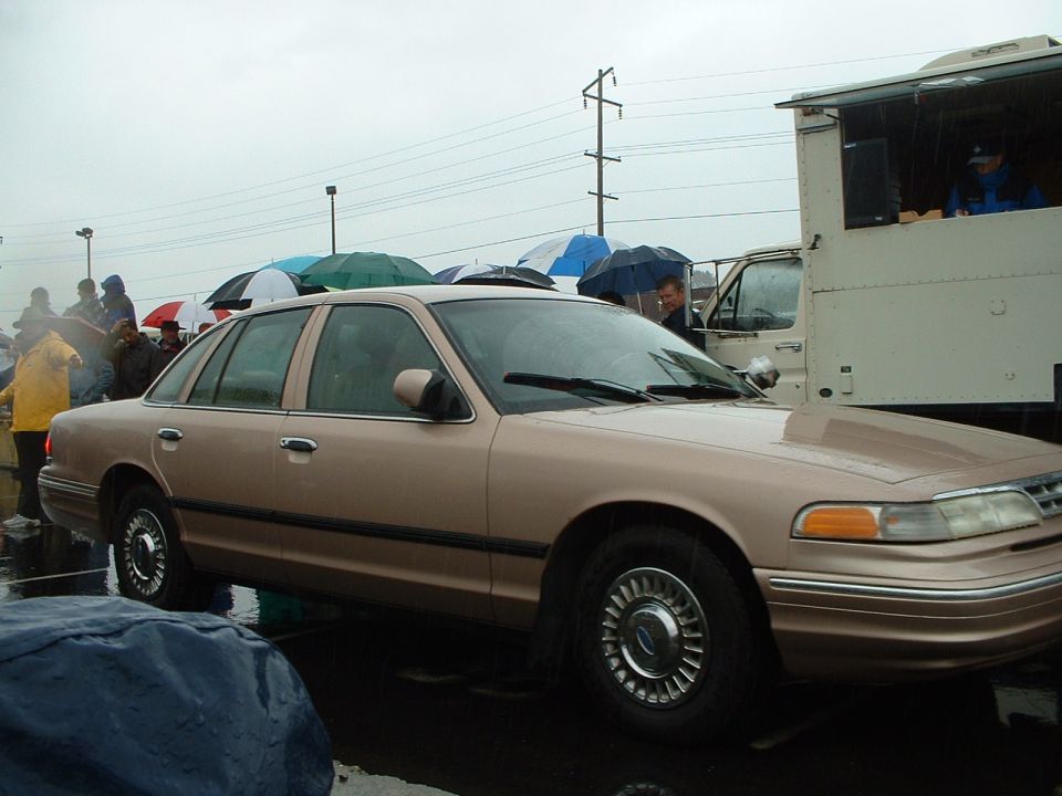 Tan Ford Crown Victoria sedan in profile on a rainy auction lot