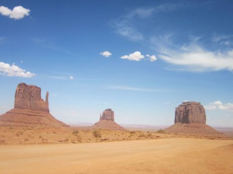 1991 Ford LTD Crown Victoria - Iconic sandstone buttes rise from the desert floor in Monument Valley under a bright, cloudy sky.