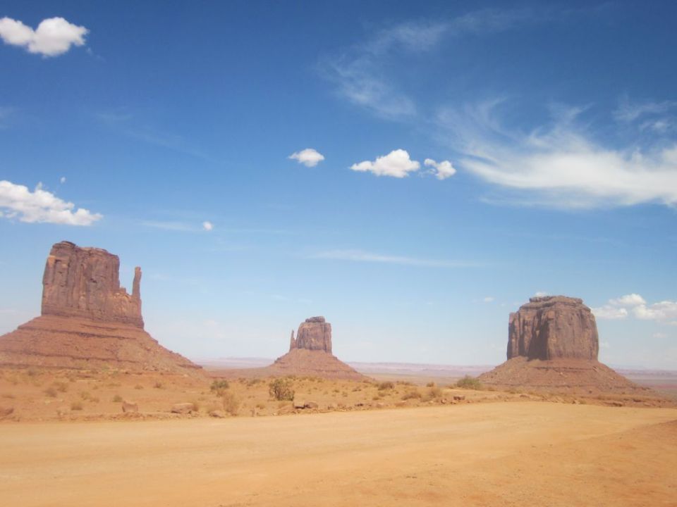 Desert landscape with rock formations under a blue sky with clouds. Watermark says SUPERMOTORS