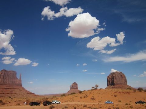 1991 Ford LTD Crown Victoria - Several vehicles are parked on a dirt road with the iconic rock formations of Monument Valley under a blue sky with white clouds.