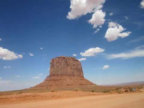 1991 Ford LTD Crown Victoria - A vast desert landscape in Monument Valley under a bright blue sky with scattered clouds, a distant white vehicle.