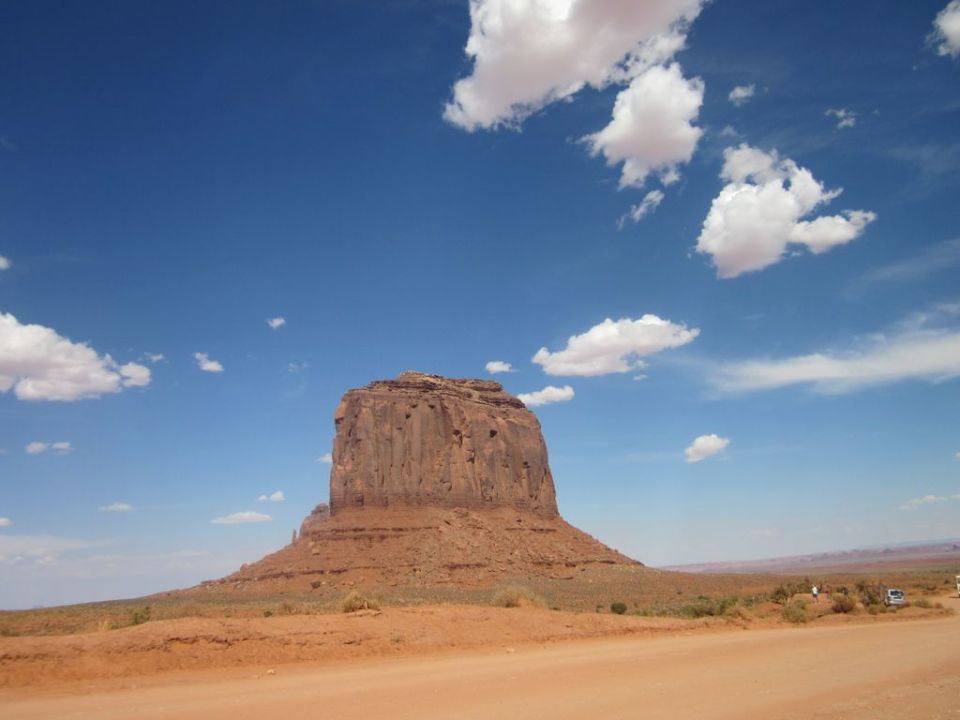Monument Valley landscape with a distant white vehicle under a blue sky