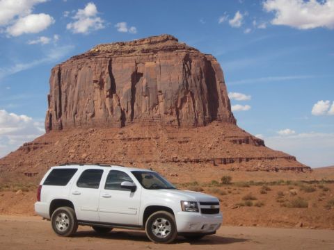 1991 Ford LTD Crown Victoria - A white SUV is parked on a dirt road in Monument Valley, with a massive sandstone butte dominating the landscape.
