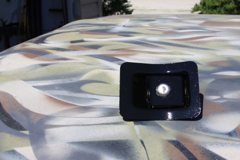 1979 Ford F-350 - A black truck hood latch is visible on a camouflage-painted surface.
