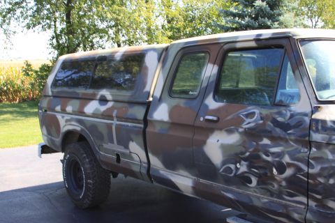 1979 Ford F-350 - This 1979 Ford F-350 pickup truck features a distinctive camouflage paint job and a camper shell, viewed from the side.