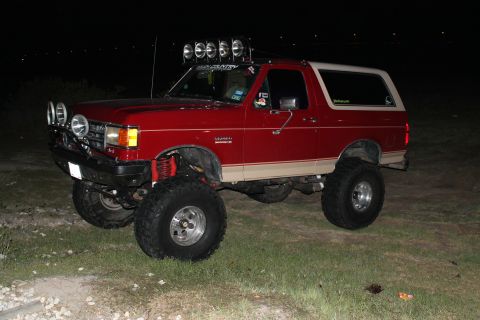 1990 Ford Bronco - This modified Ford Bronco features a lifted suspension and numerous lights, suggesting off-road use.