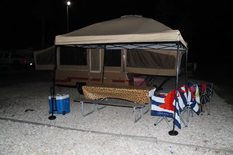 1990 Ford Bronco - A pop-up camper is set up at a campsite, complete with a picnic table and chairs, ready for outdoor enjoyment.