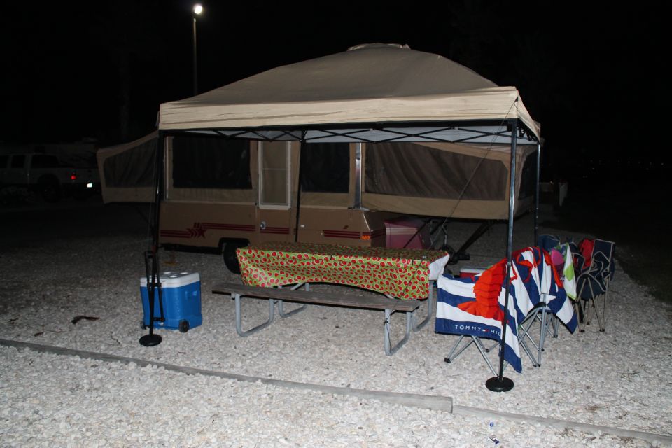 Pop-up camper set up at campsite with picnic table and chairs
