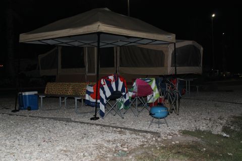 1990 Ford Bronco - A campsite is set up at night with a pop-up tent, chairs, a cooler, and a small grill visible.