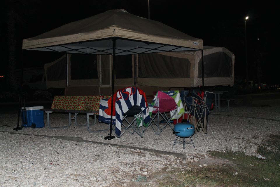 campsite setup at night with pop-up tent, chairs, cooler, and grill