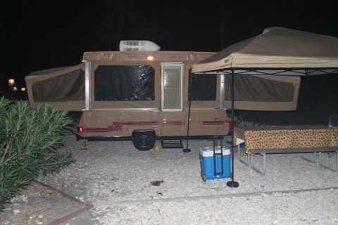 1990 Ford Bronco - A pop-up camper is set up at a campsite with a cooler and picnic table visible.