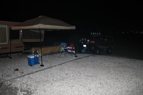 1990 Ford Bronco - A red SUV with multiple off-road lights is parked at a campsite next to a pop-up trailer and a canopy.