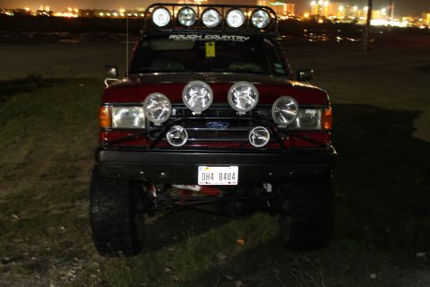 1990 Ford Bronco - This red Ford Bronco is equipped with a roof-mounted light bar and additional bumper lights, ready for off-road adventures.