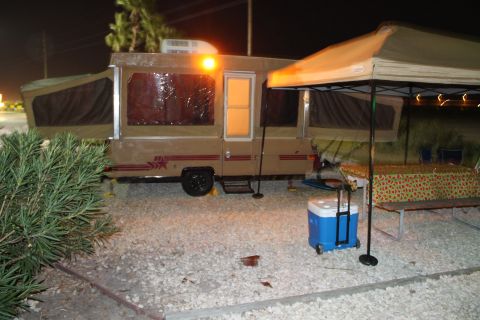 1990 Ford Bronco - A pop-up camper is set up at a campsite with an awning providing shade over a table and cooler.